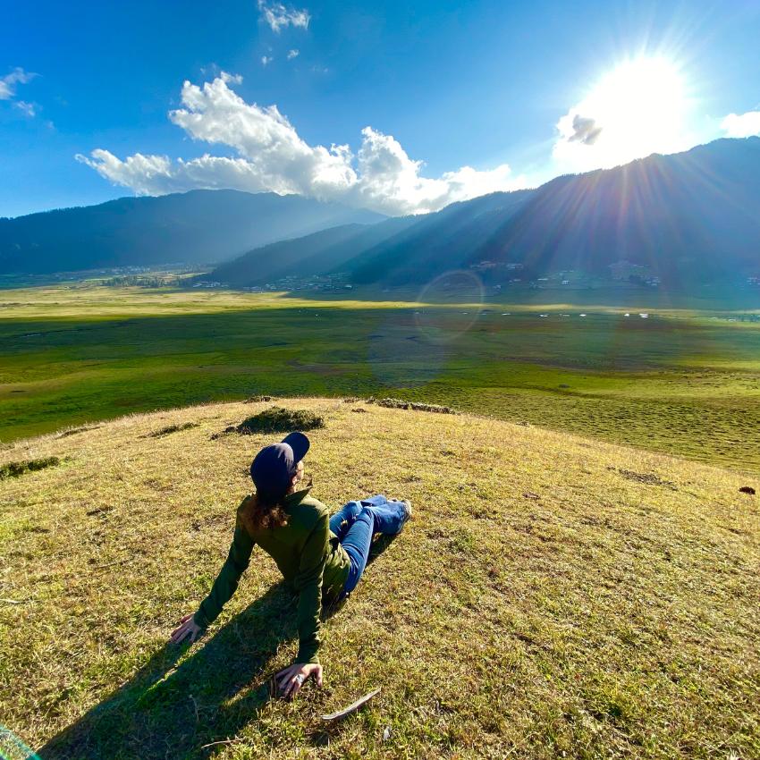 Kati Jalali sitting in a valley looking at mountains and sun focusing on stress management